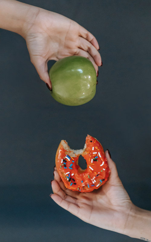 Eine Hand hält einen Apfel und eine Hand hält einen Donut